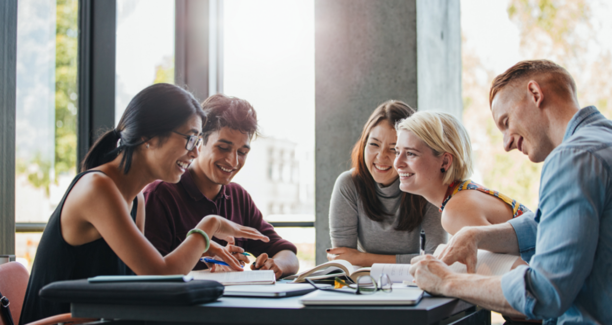 Several students studying and laughing with notebooks at a table