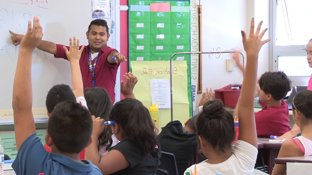 Teacher in an elementary classroom pointing to a student with their hand raised.