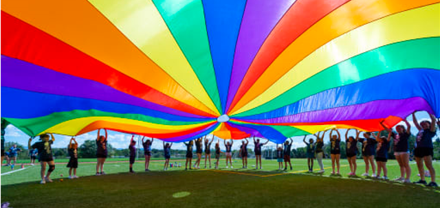 Students standing under a rainbow colored fabric lit by the sun