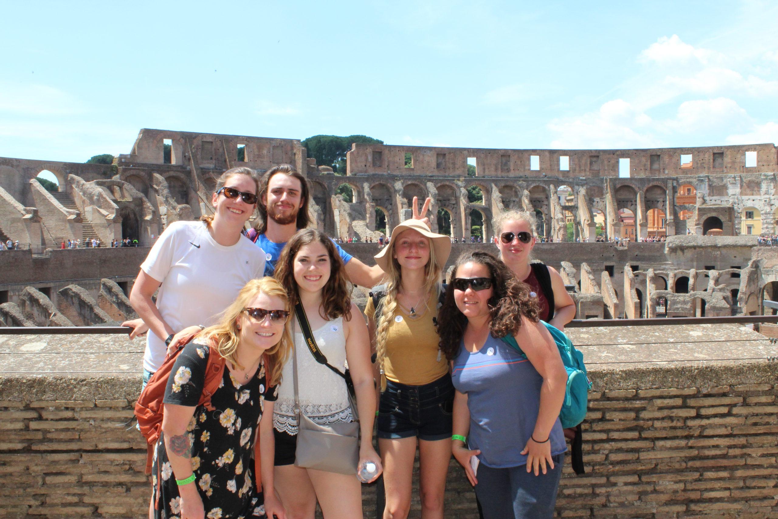 six women and one man posing in front of the colosseum in rome, italy