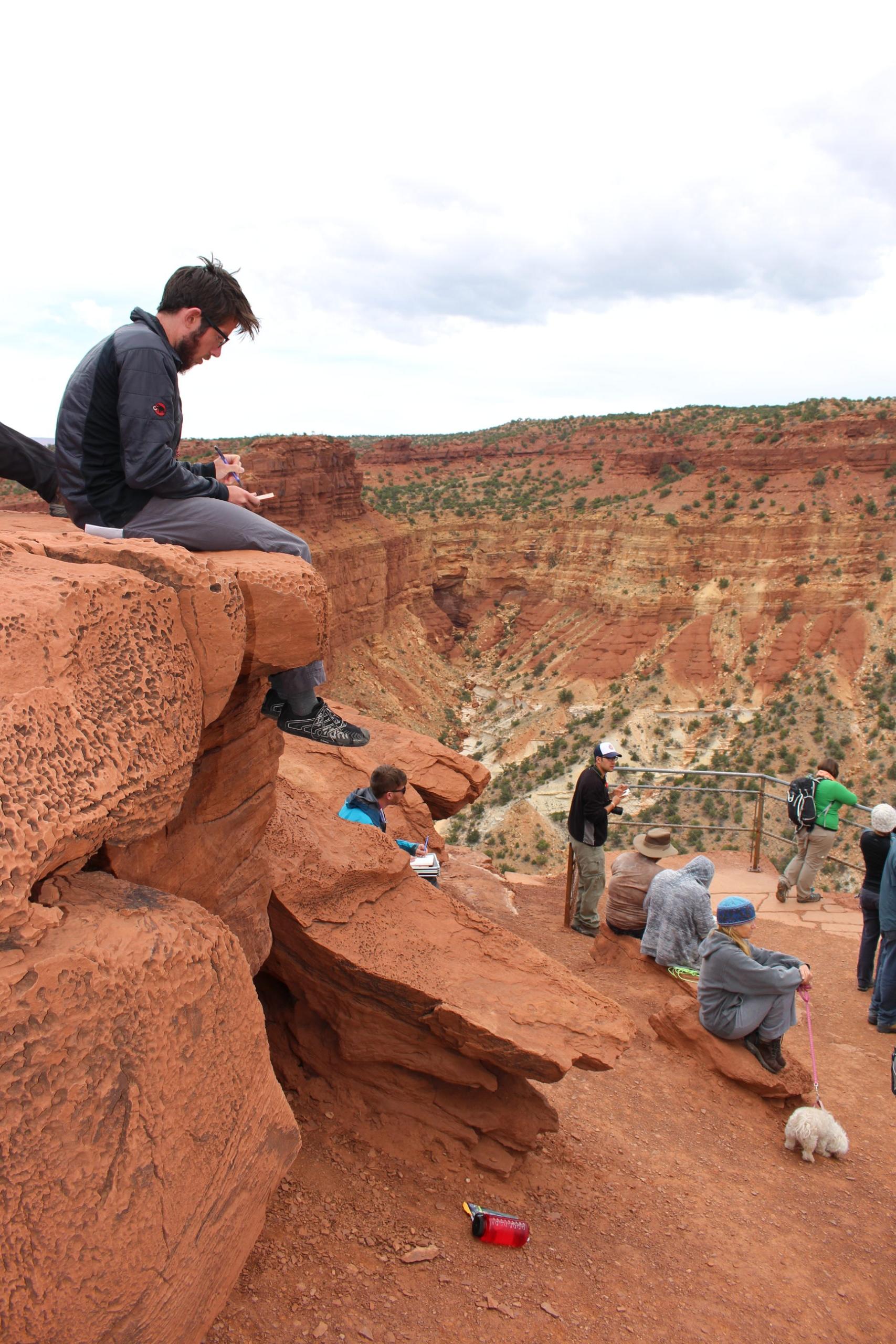 Students taking notes while sitting on cliff edges overlooking a valley