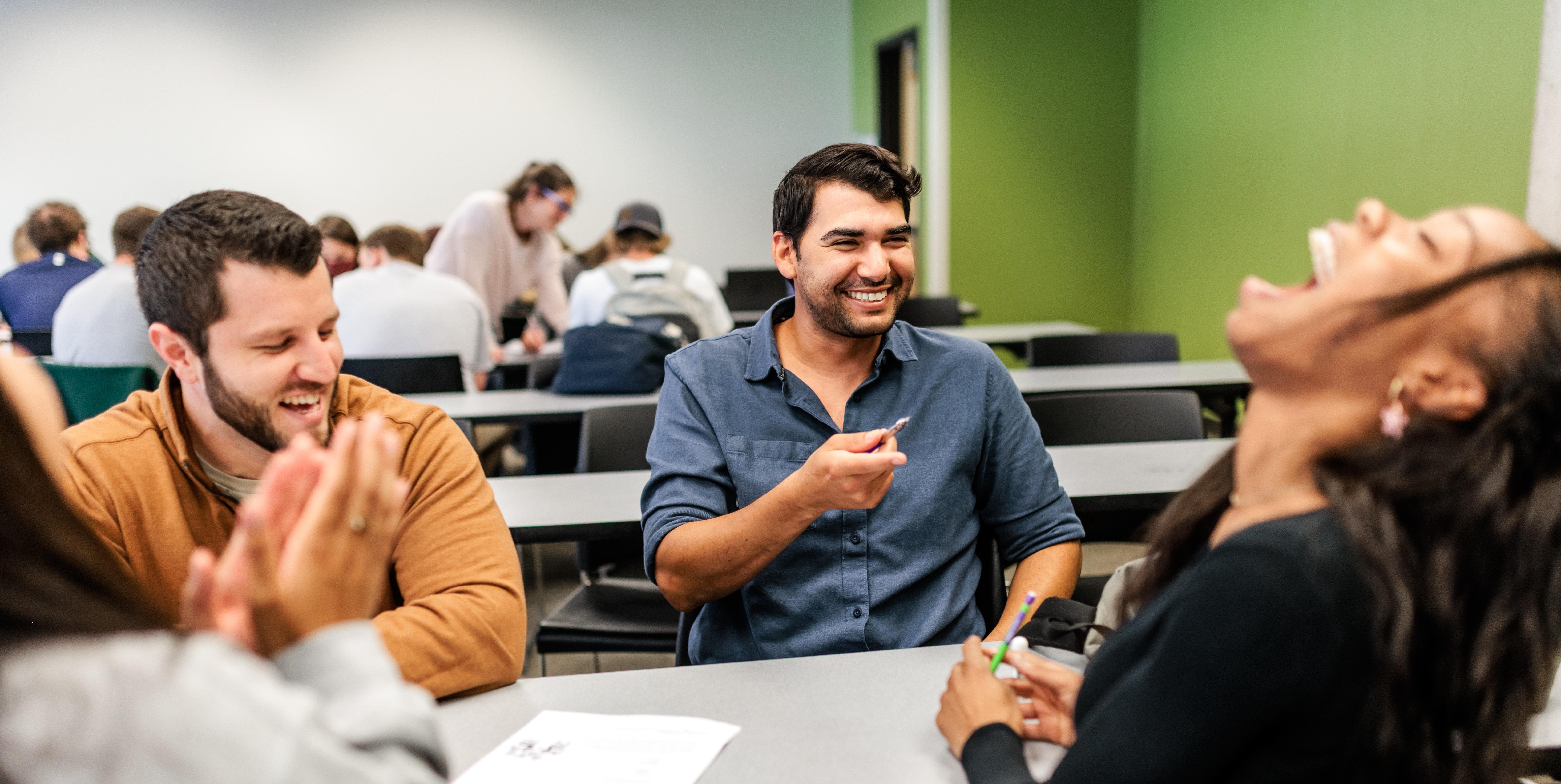 Three students laugh while working in a classroom