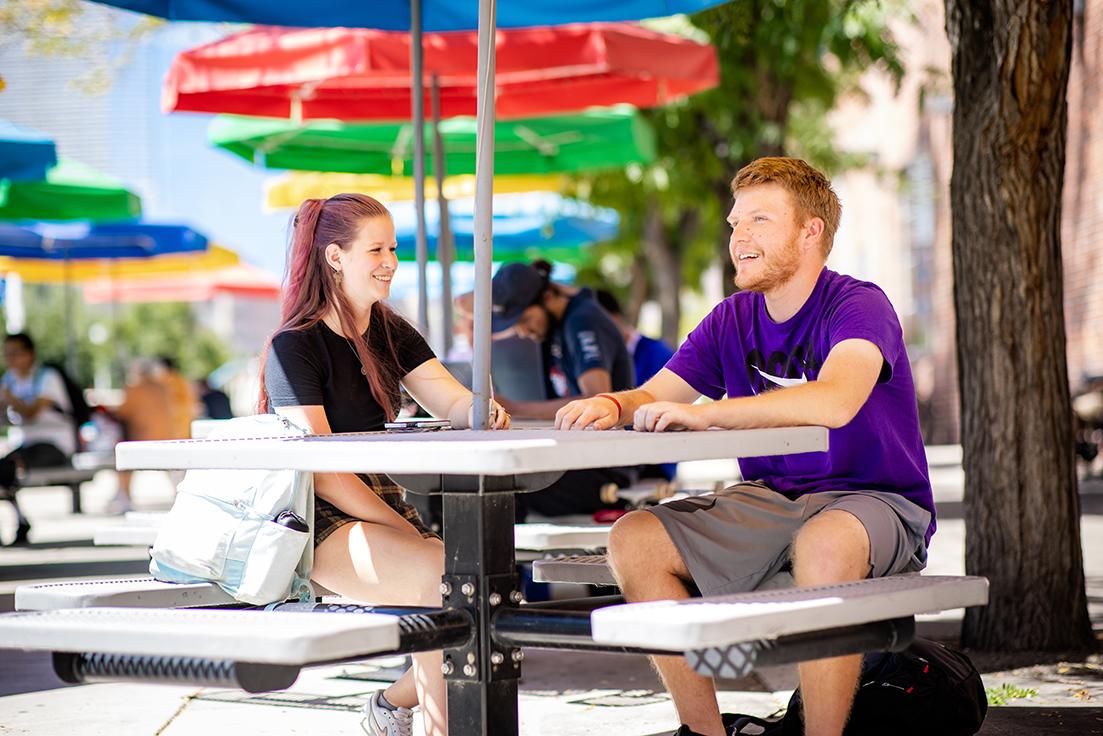 Two students sitting at an outdoor picnic table outside of the Tivoli