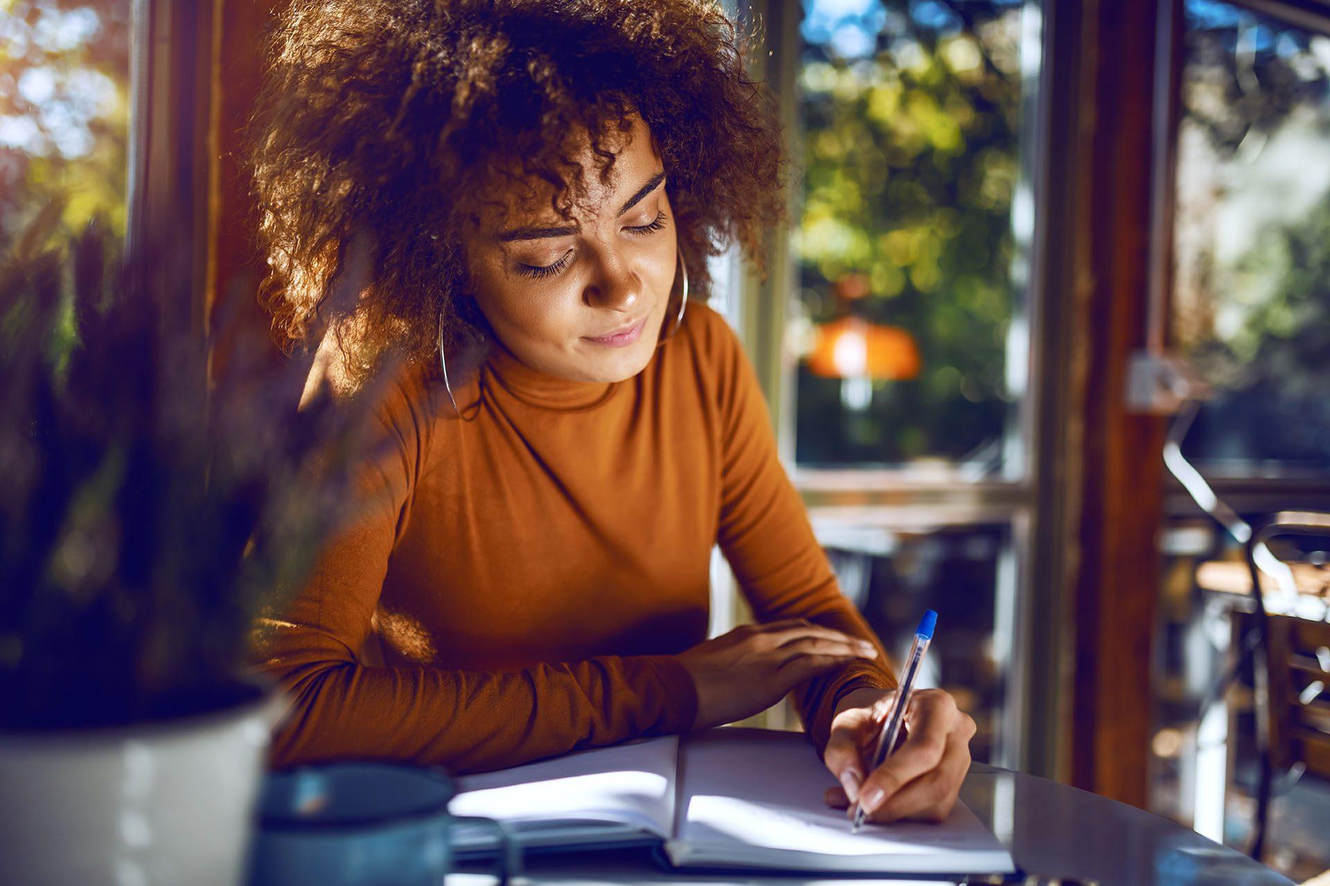 Portrait of cute mixed race student with curly hair and in turtleneck sitting in cafe and studying for exams.