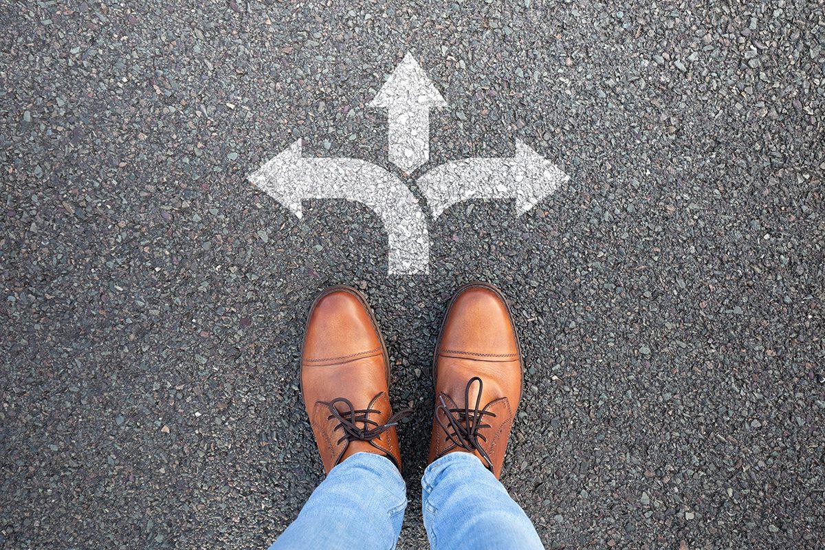 Person standing on asphalt with arrows pointing various directions