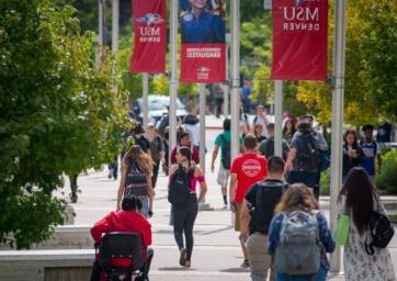 Students walking on campus near flagpoles with MSU Denver banners